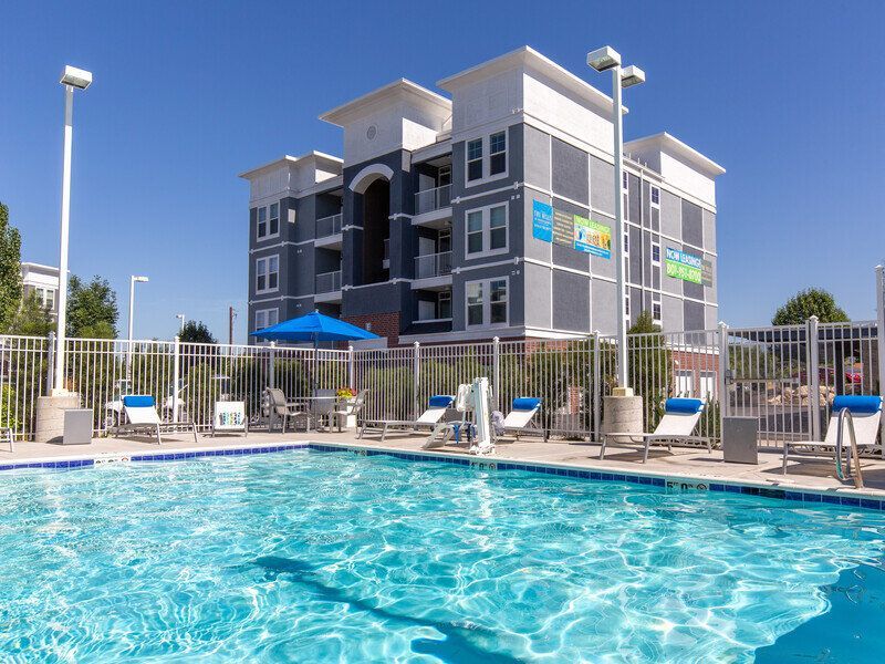 Outdoor pool area with lounge chairs and a gated apartment building in the background.
