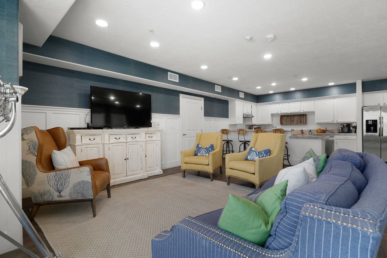 Bright open-concept living room with blue accents, a TV, and a kitchen in the background.