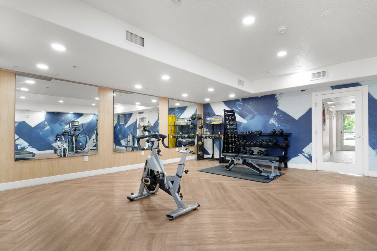 Indoor apartment gym with cardio bike, free weights, and mirrored wall.