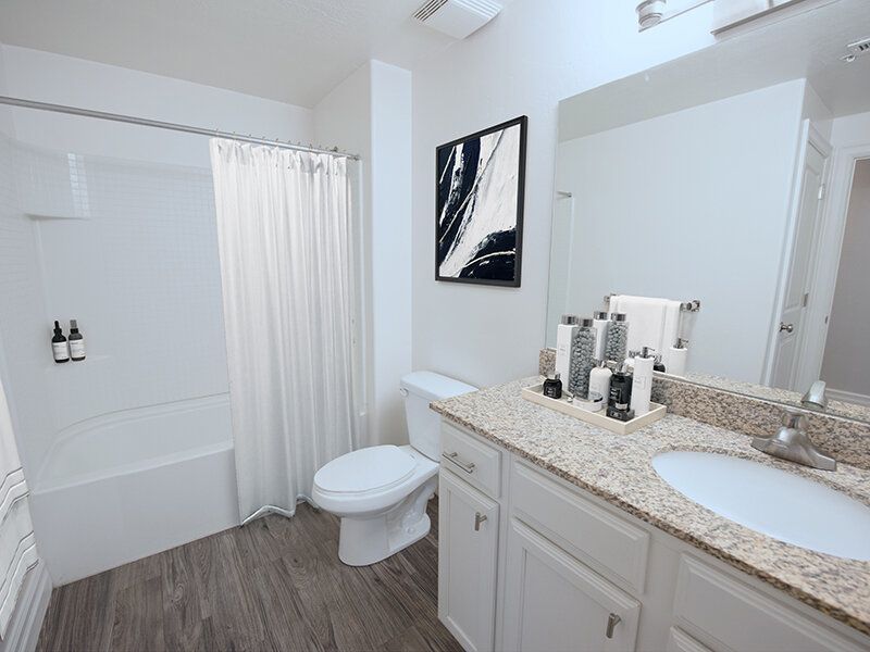 Modern apartment bathroom with granite vanity, sink, toilet, and shower/tub.