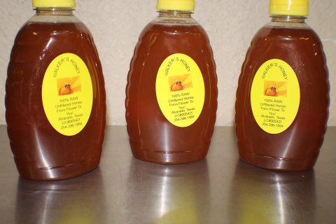 Three honey bottles with yellow labels on a reflective surface.