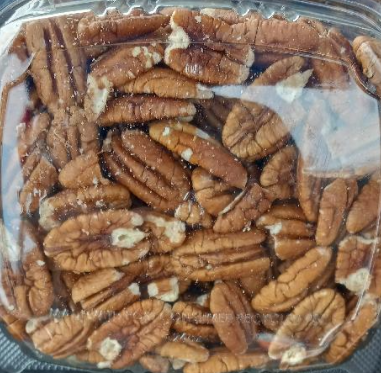 Pecan nuts on a wooden board, with a coconut shell, nutcracker, and burlap, against a dark background.