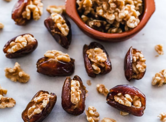 Dates filled with walnuts, scattered on a white surface, with a small bowl of walnuts.