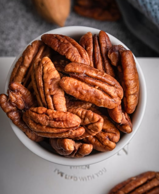 White bowl filled with brown pecan halves, close-up on a white surface.