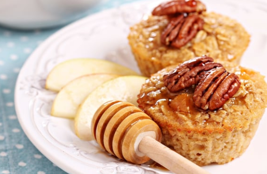 Oatmeal muffins topped with pecans and syrup on a plate with apple slices and a honey dipper.