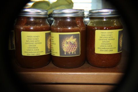 Three jars of honey, labeled with product descriptions, on a wooden shelf.