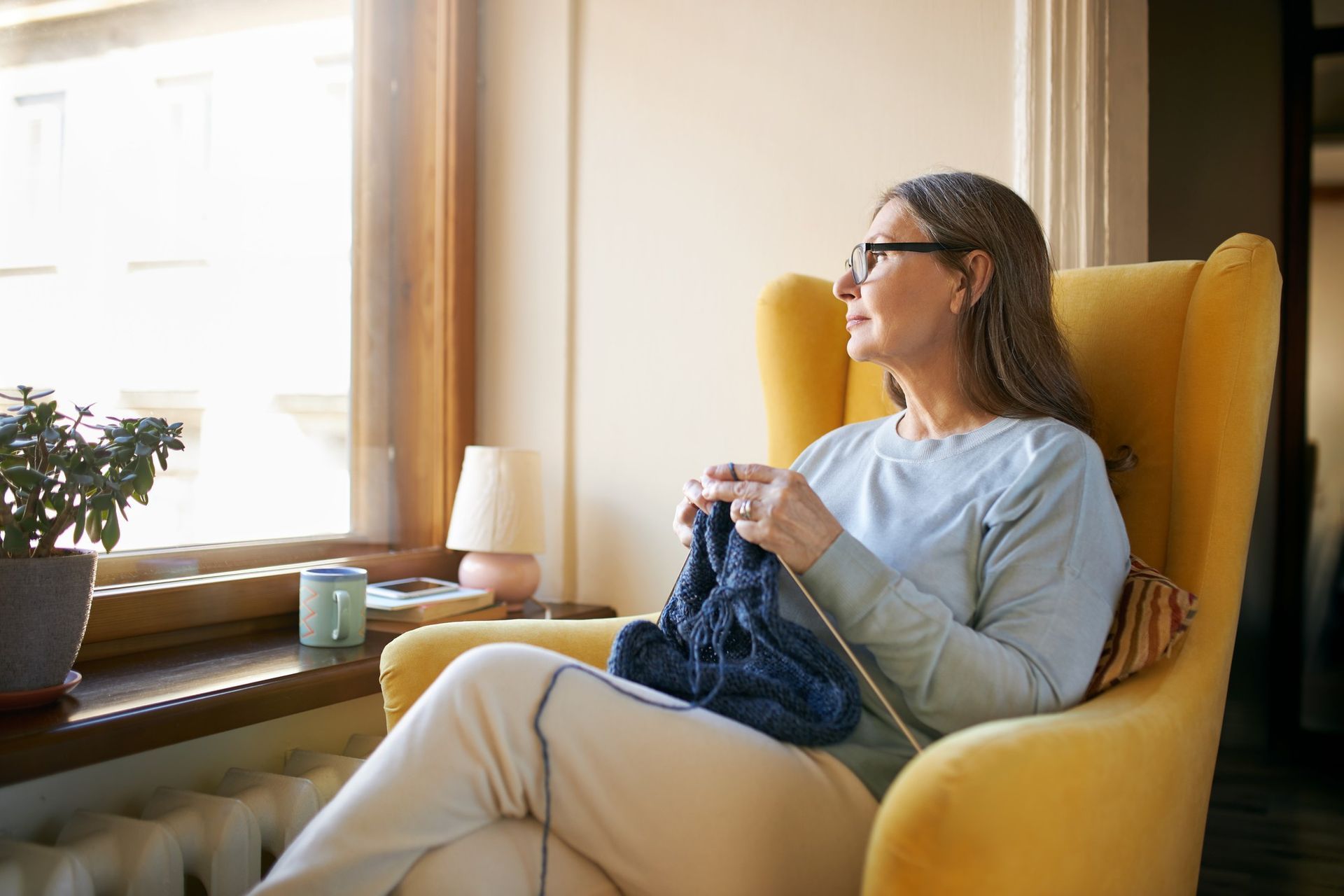 Person knitting in a yellow armchair by a sunlit window
