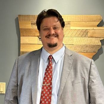 A man in a suit and tie is standing in front of a wooden map.