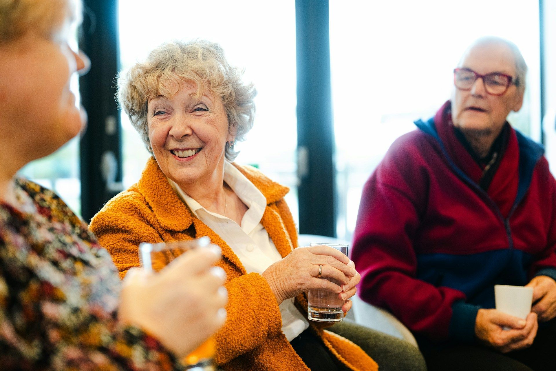 Three people chatting and smiling while holding cups in a bright indoor gathering