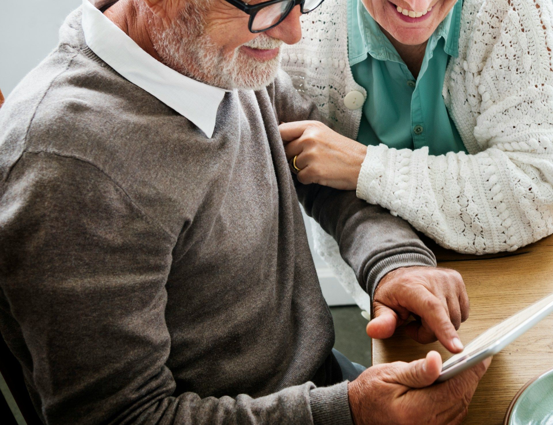Two people smiling over a smartphone at a table, with a tablet nearby.
