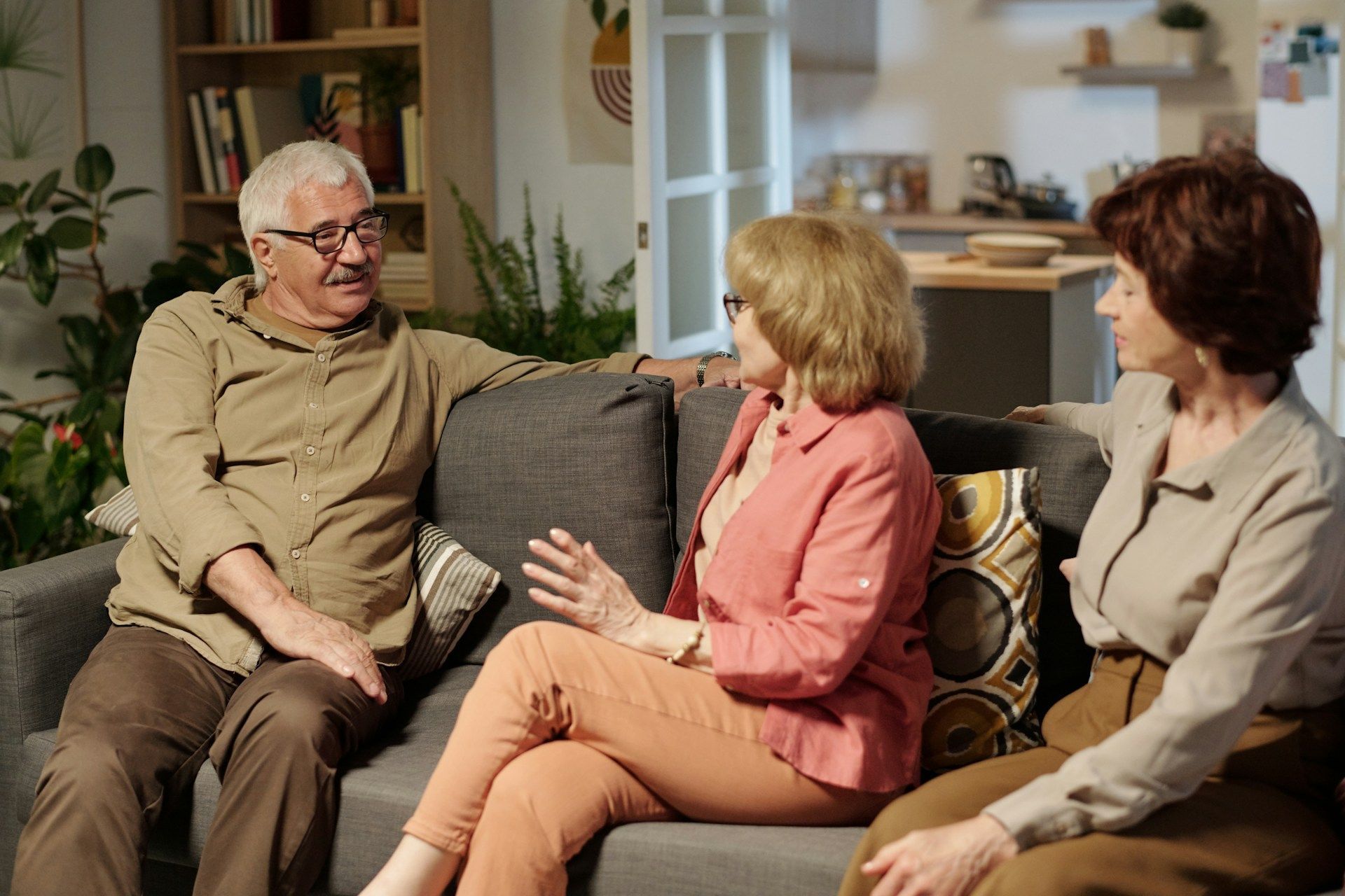 Three people sitting on a couch in a living room, talking together.