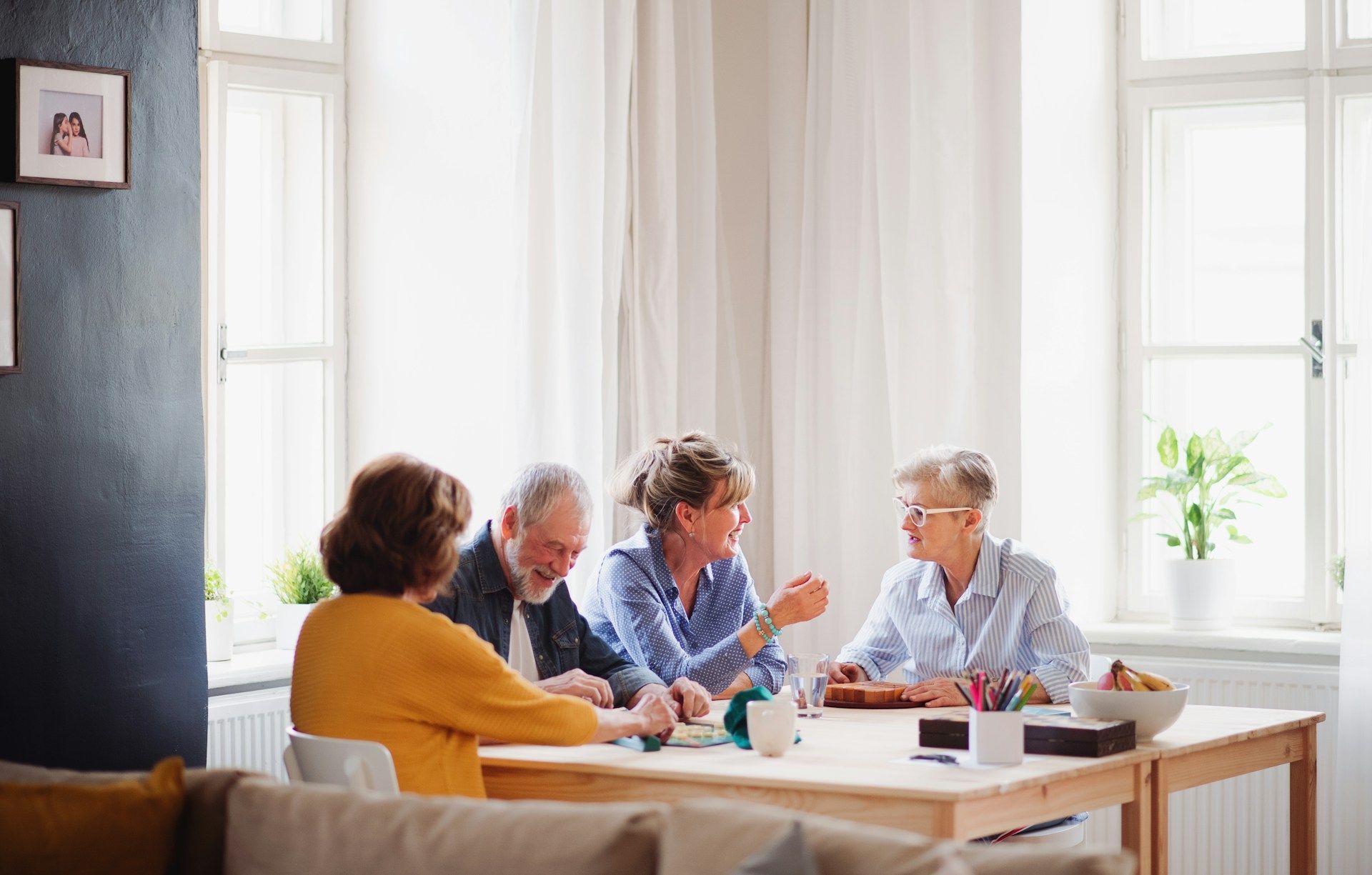 Four people in a bright room discussing papers around a table by large windows