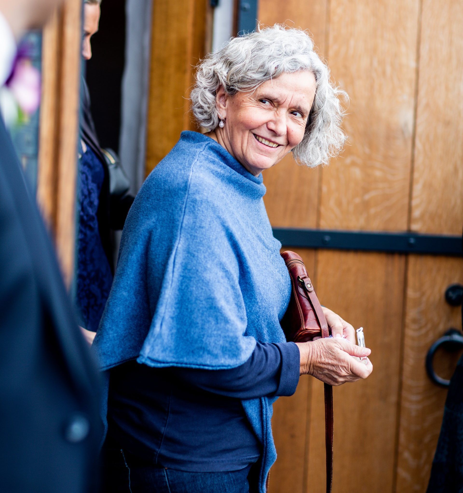 A woman in a blue poncho is smiling and holding a brown purse