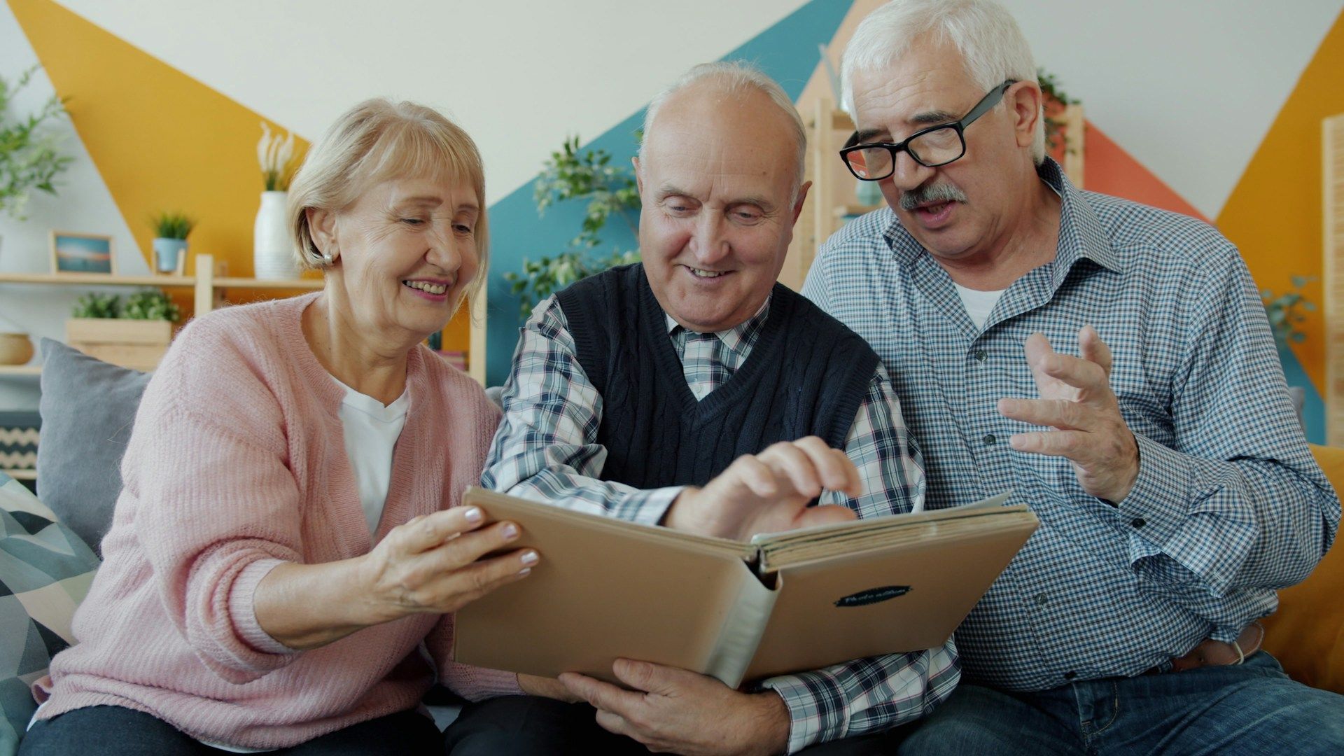 Three smiling people looking at a tablet on a couch in a bright room