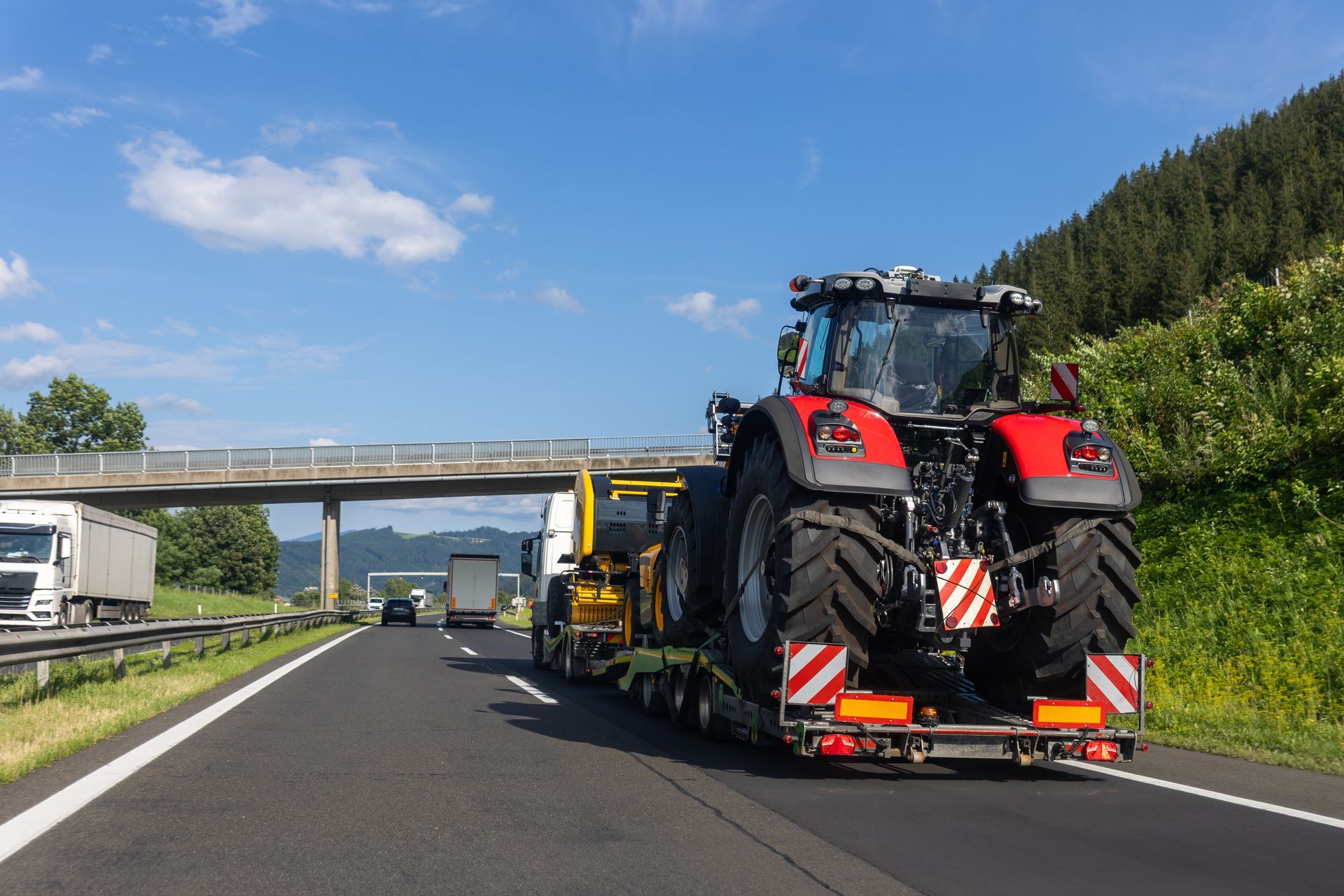 Heavy duty road services transporting agricultural tractor on trailer along highway route. Heavy duty road services transporting agricultural tractor on trailer along highway route.