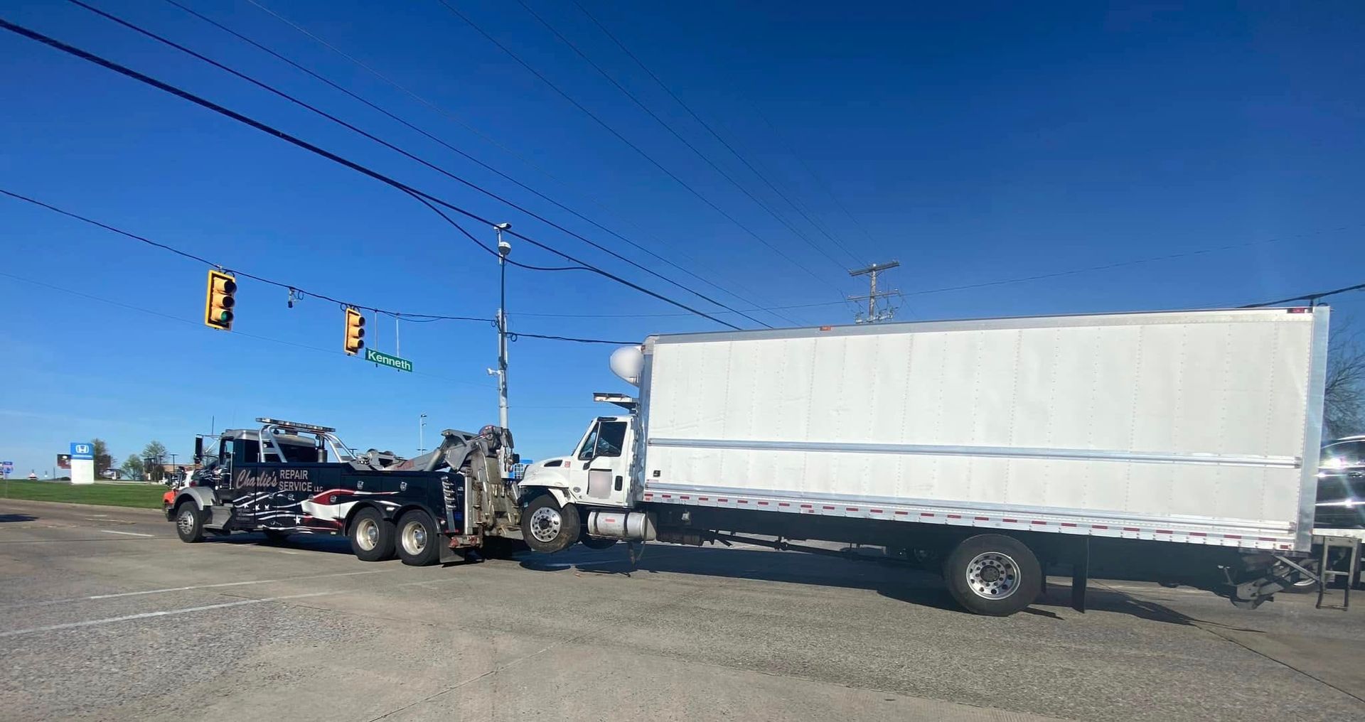 A tow truck towing a large white box truck on a clear, sunny day.