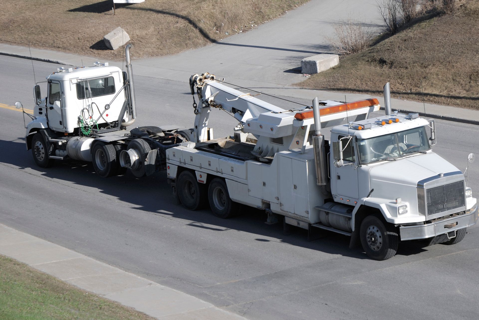 Tow truck towing a white semi-truck cab on a paved road.