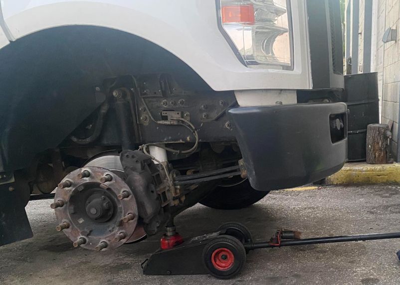 A white truck raised on a jack; front tire removed, showing the brake assembly. A white truck raised on a jack; front tire removed, showing the brake assembly.