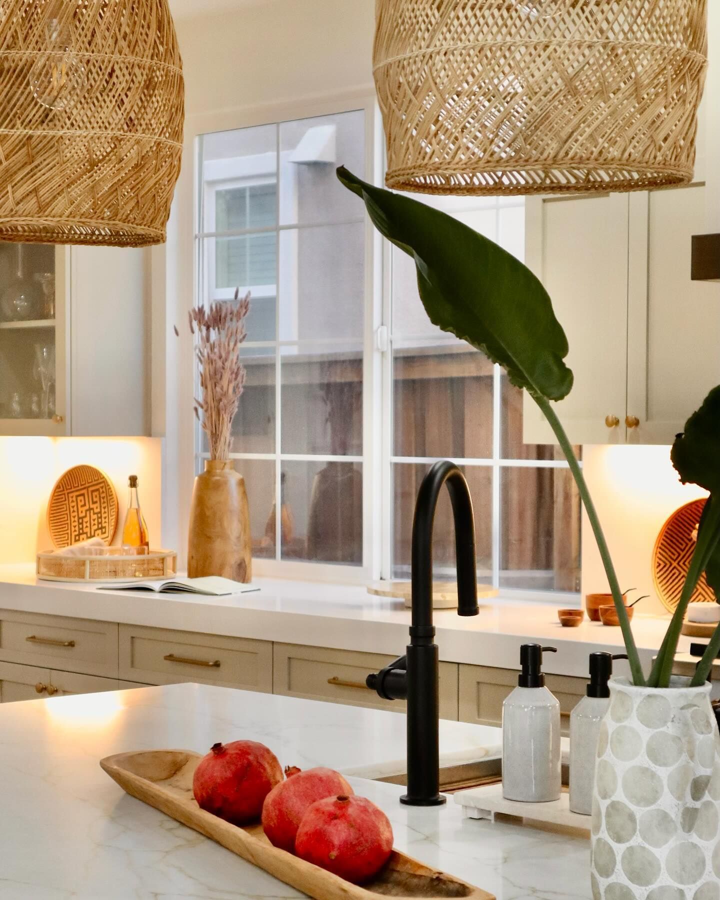 Kitchen with woven pendant lights, black faucet, and fruit in a wooden bowl on a marble countertop.
