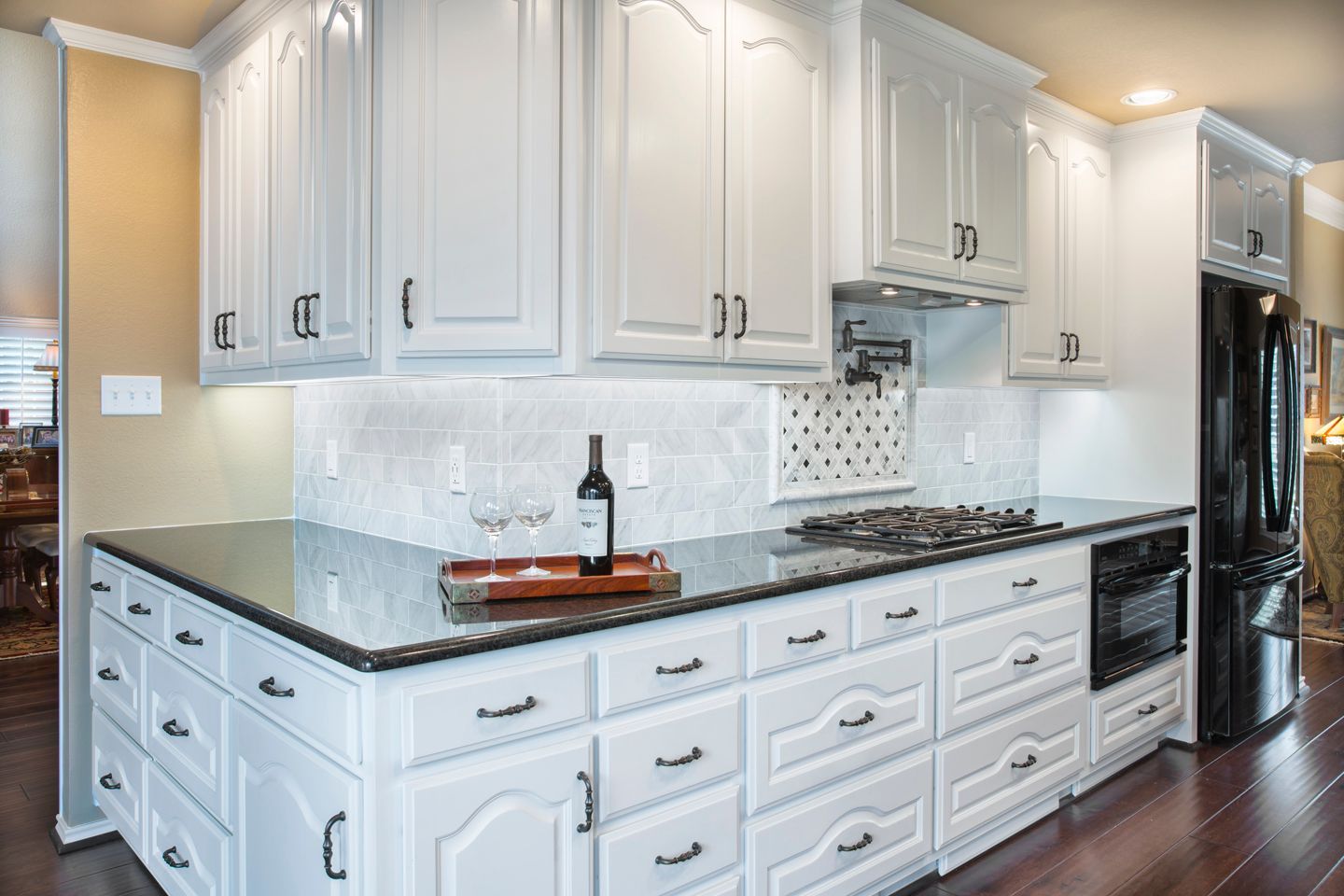White kitchen cabinets with black countertops and appliances, wood flooring.