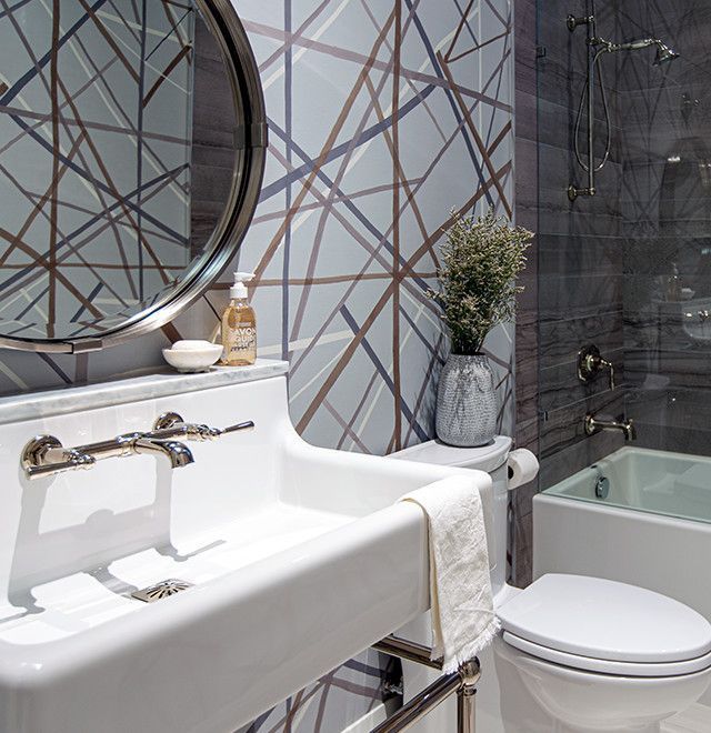 Bathroom with geometric wallpaper, white sink, round mirror, and a small bathtub.