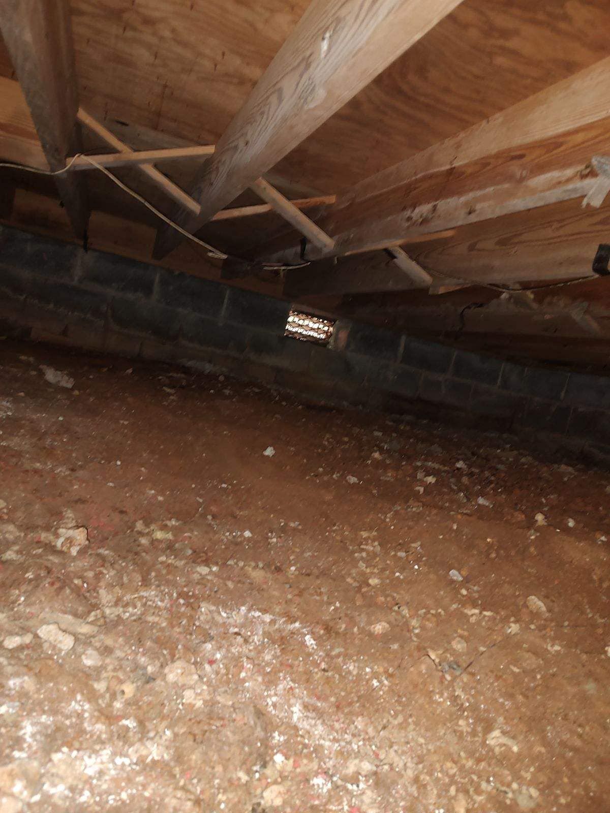 A crawl space underneath a house with a lot of dirt and rocks.