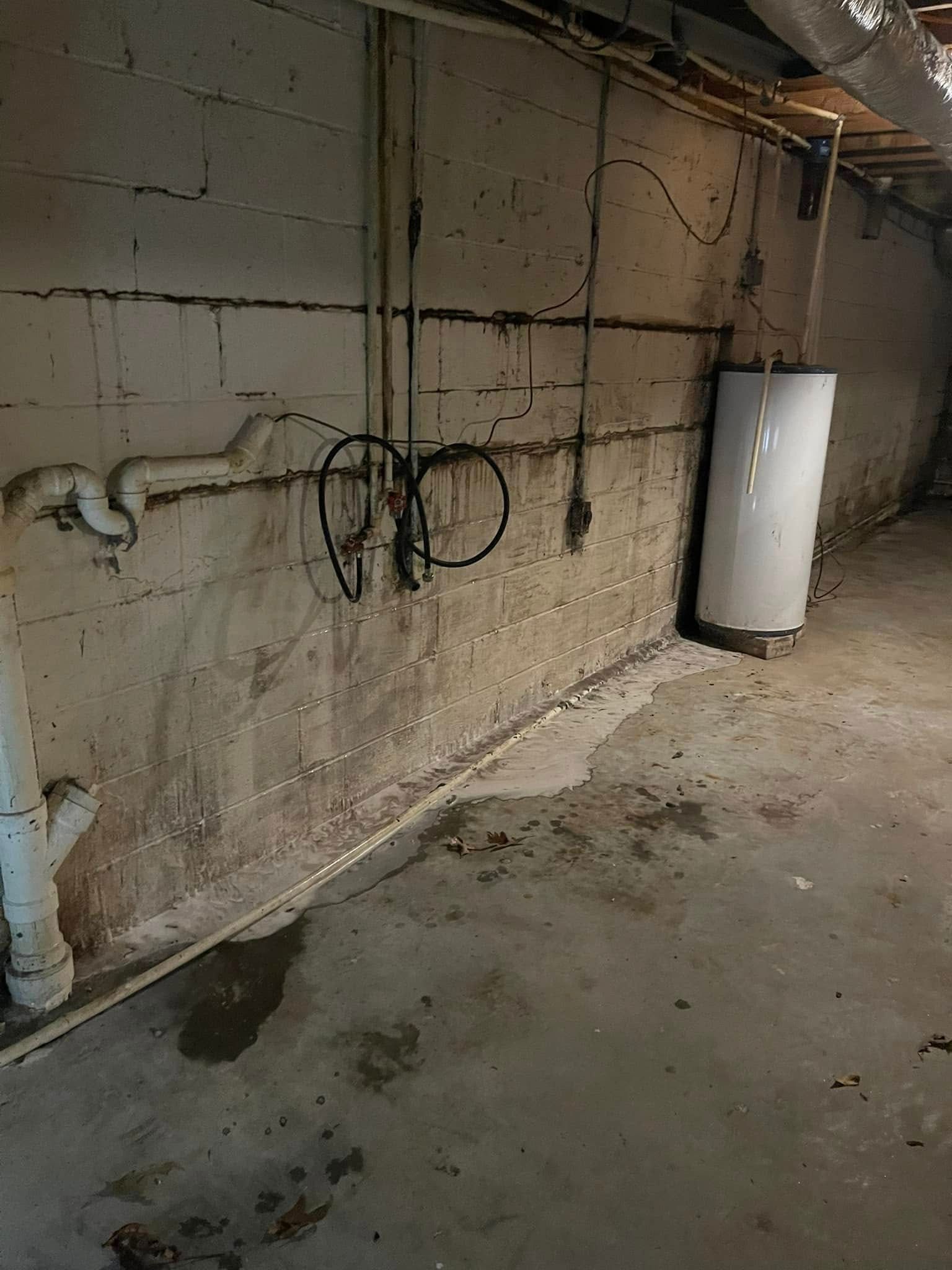 A dirty basement with a water heater and pipes on the wall.