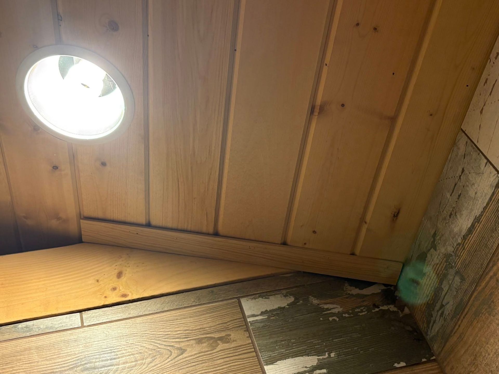 A corner of a wooden room with a light on the ceiling.