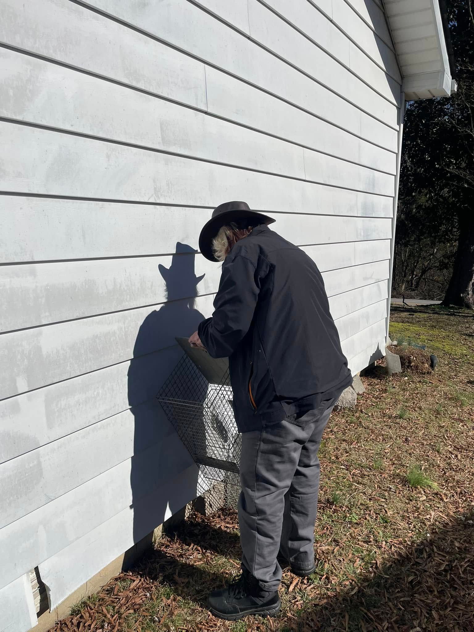 A man in a cowboy hat is standing in front of a white house.