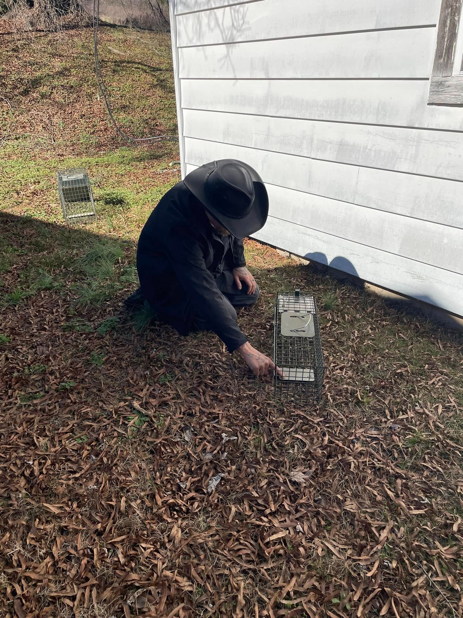 A man in a hat is kneeling on the ground in front of a white house.