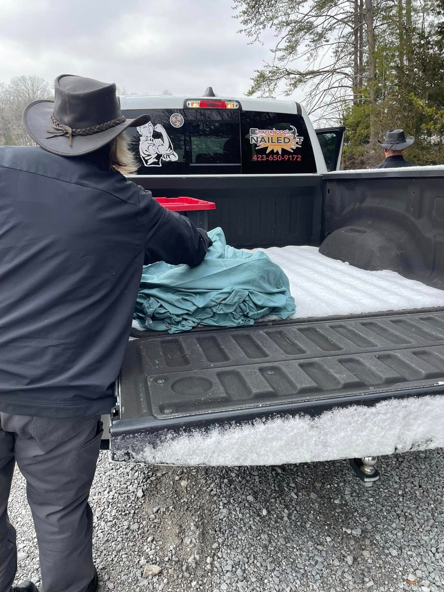 A man in a cowboy hat is loading clothes into the back of a truck.