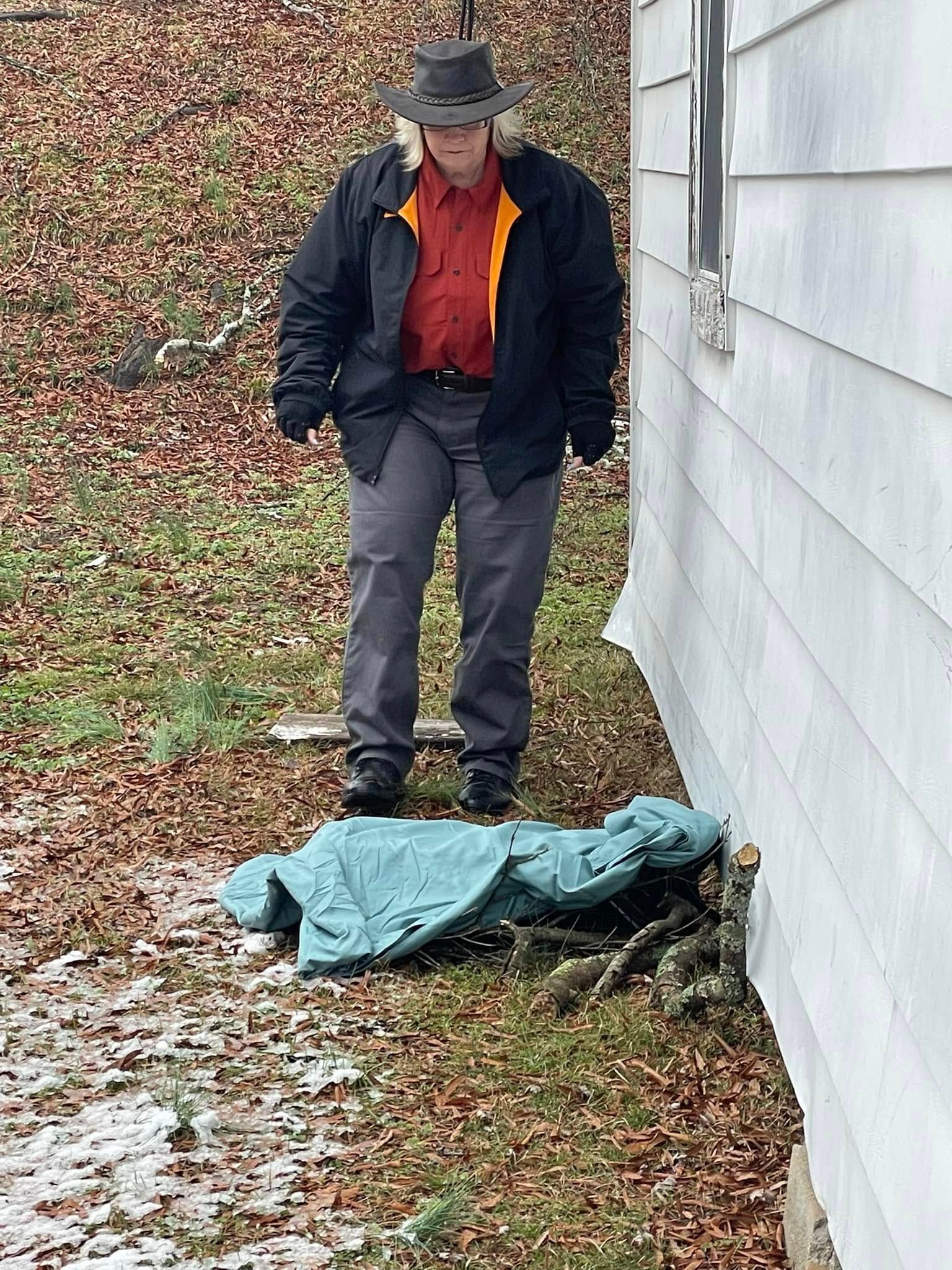 A man in a hat is standing next to a house.
