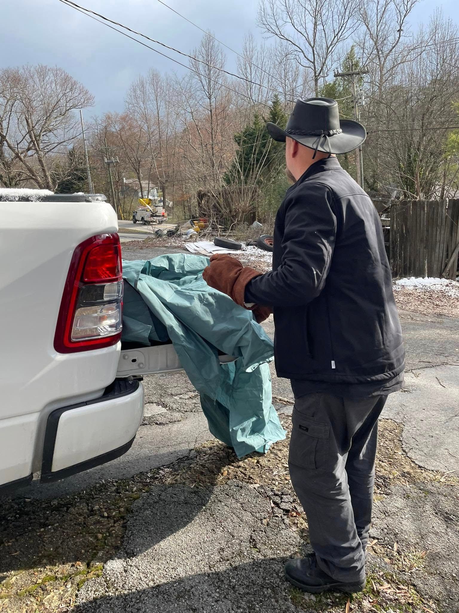 A man in a cowboy hat is putting a tarp in the back of a truck.