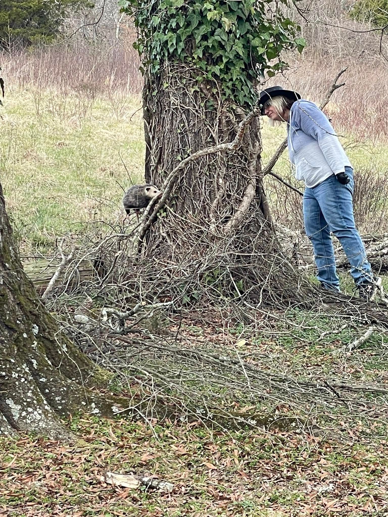 A woman is standing next to a tree in a field.