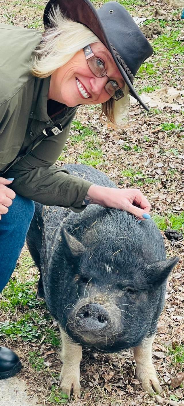 A woman in a cowboy hat is petting a pig.