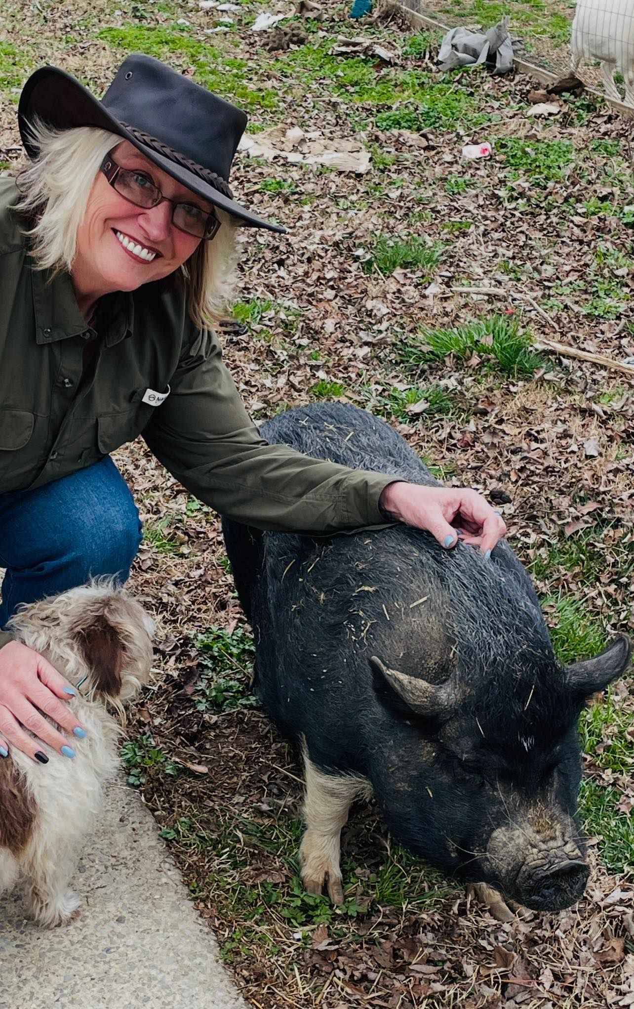 A woman in a cowboy hat is petting a pig in a field.