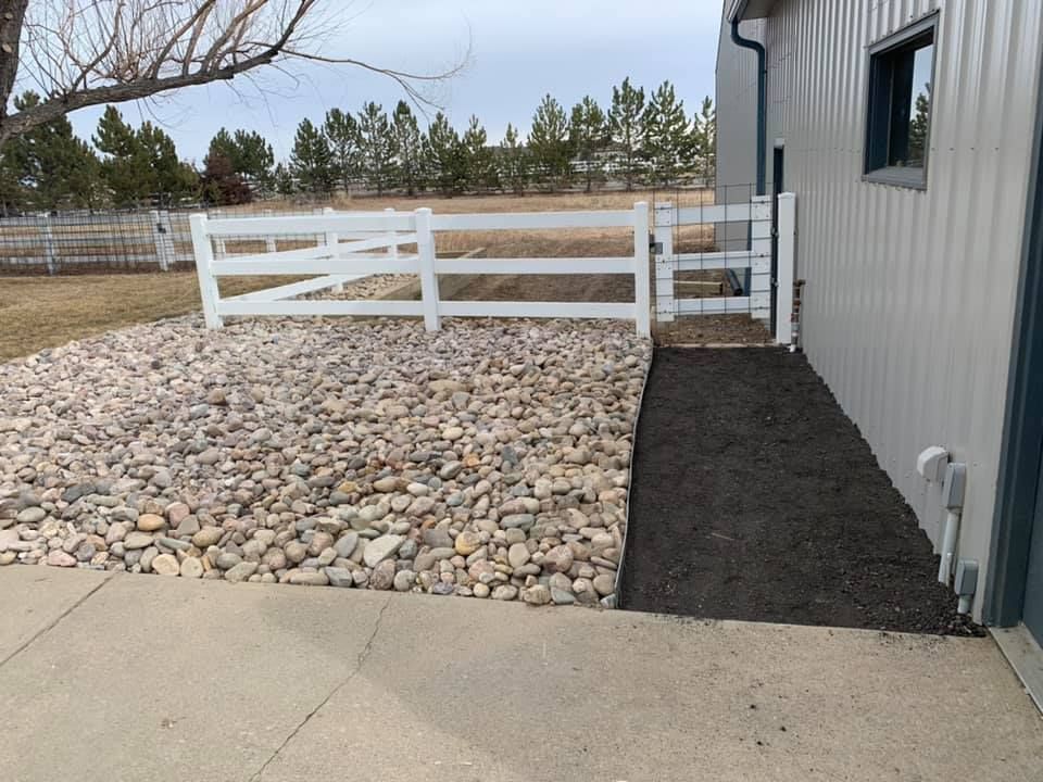 A white fence is surrounded by rocks in front of a building