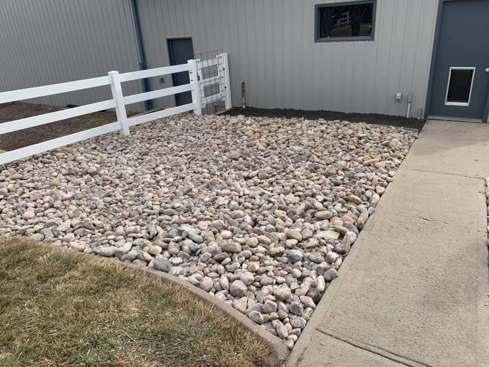 A white fence surrounds a pile of rocks in front of a building.
