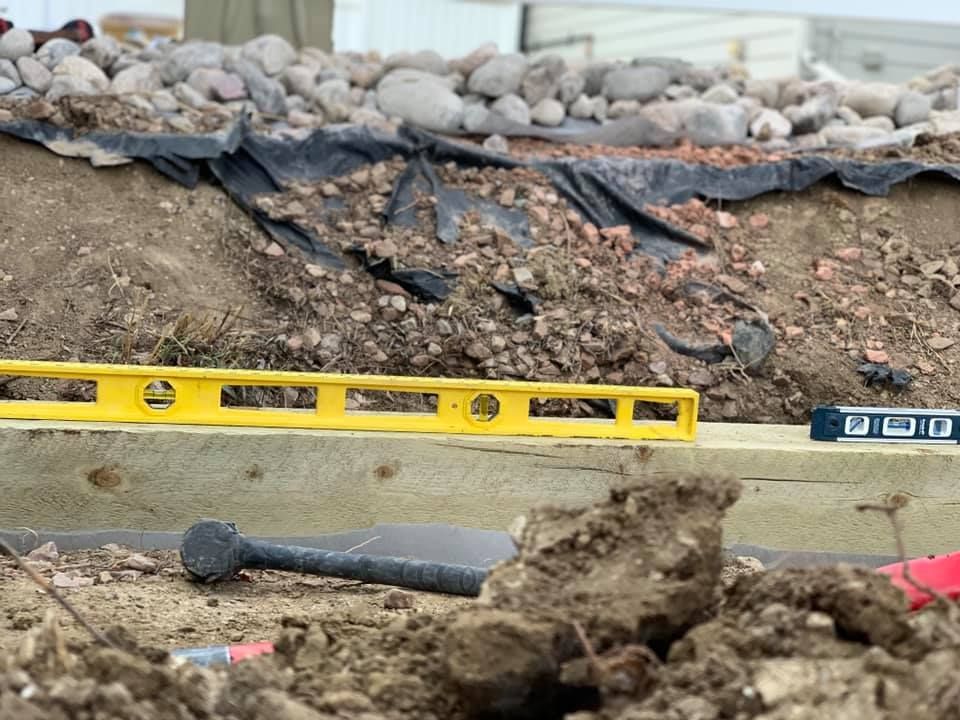 A yellow level is sitting on top of a wooden plank in the dirt.