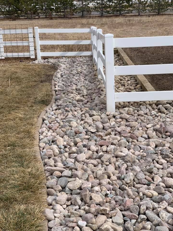 A white fence is surrounded by rocks in a yard.
