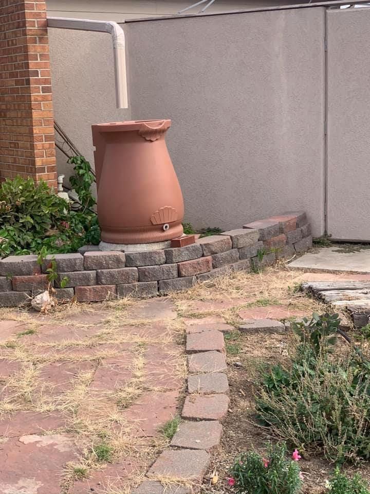 A rain barrel is sitting on a brick wall next to a brick walkway.
