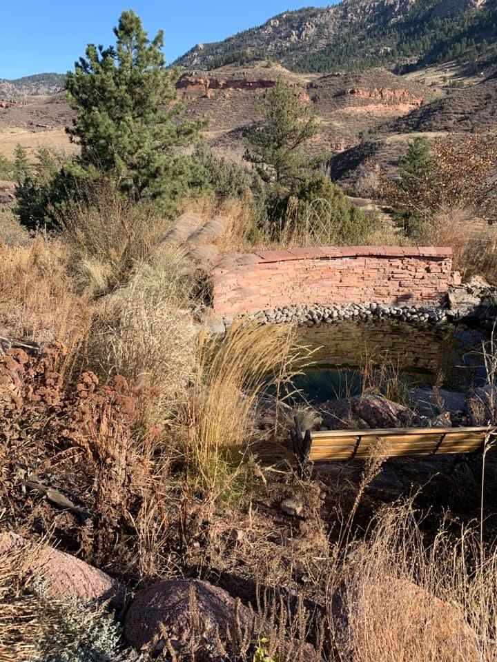 A bridge over a river in the middle of a field with mountains in the background.