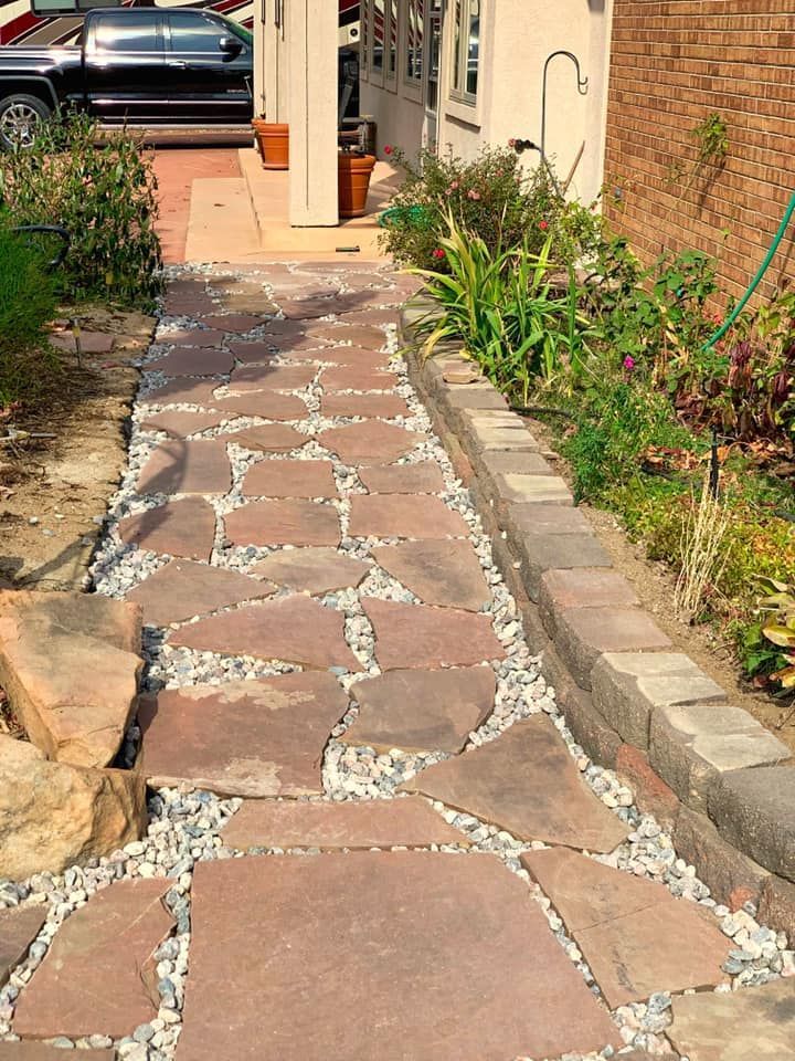A stone walkway leading to a house with a car parked in the background.