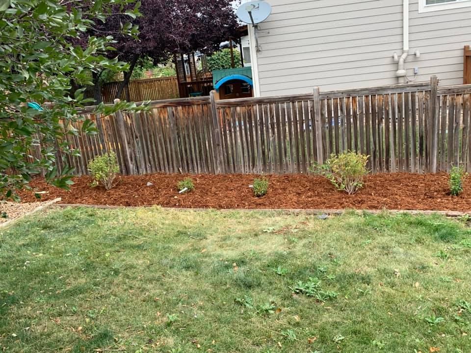 A backyard with a wooden fence and a pile of mulch.