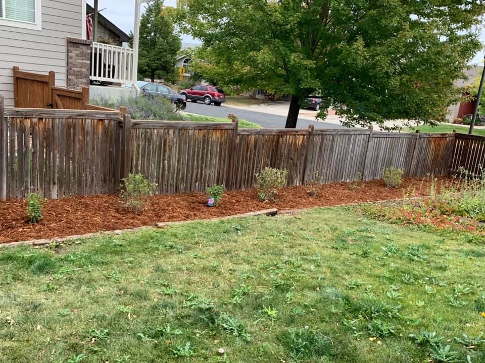 A wooden fence surrounds a lush green yard in front of a house.