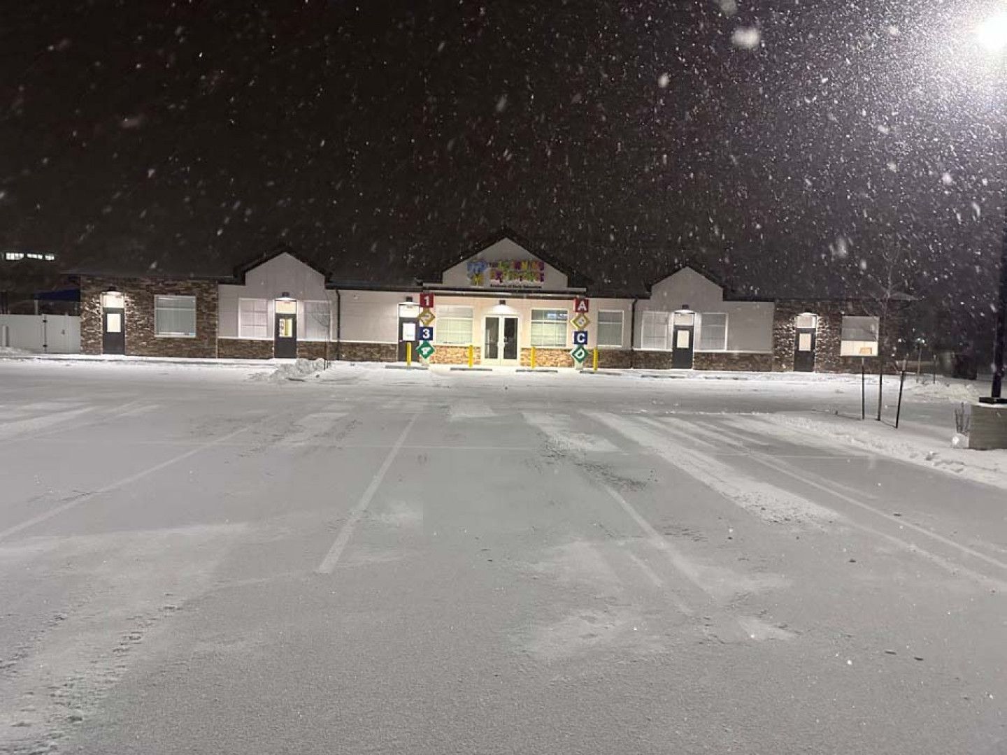 A snowy parking lot in front of a building at night.
