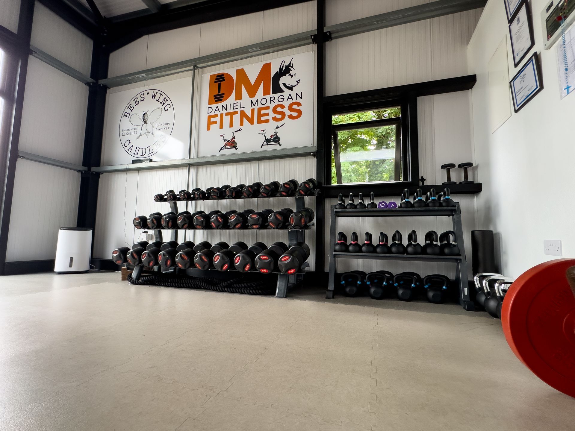 Gym interior with dumbbell racks, fitness equipment, and a Daniel Morgan Fitness sign.