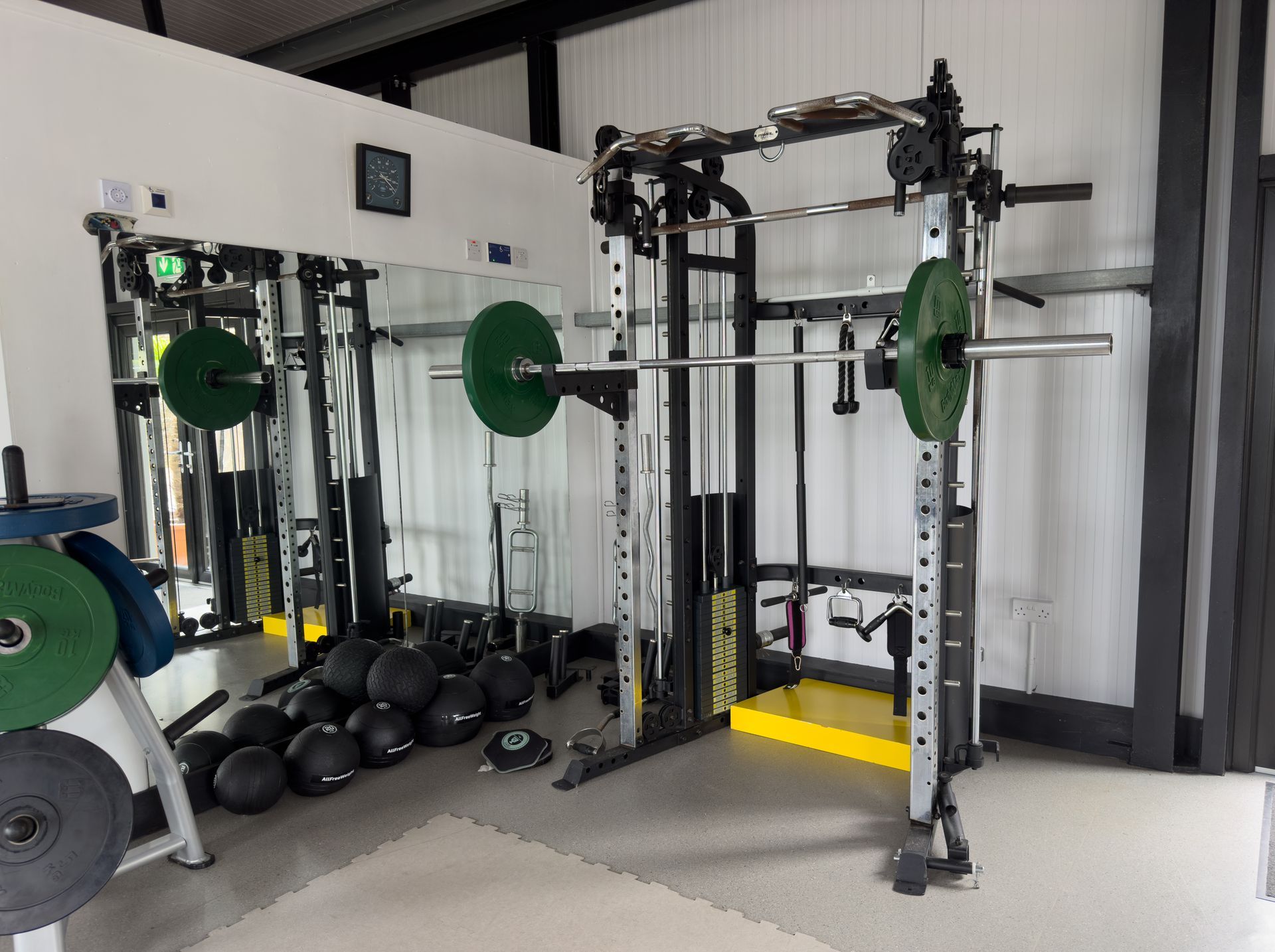 Home gym with weightlifting equipment, including a squat rack, weights, and medicine balls.