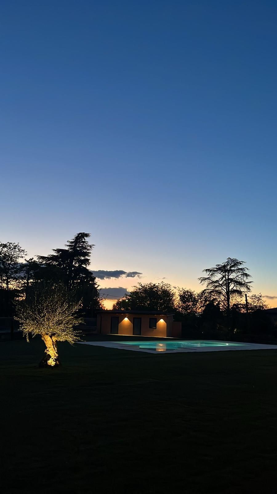 Una piscina illuminata di notte con il tramonto sullo sfondo.