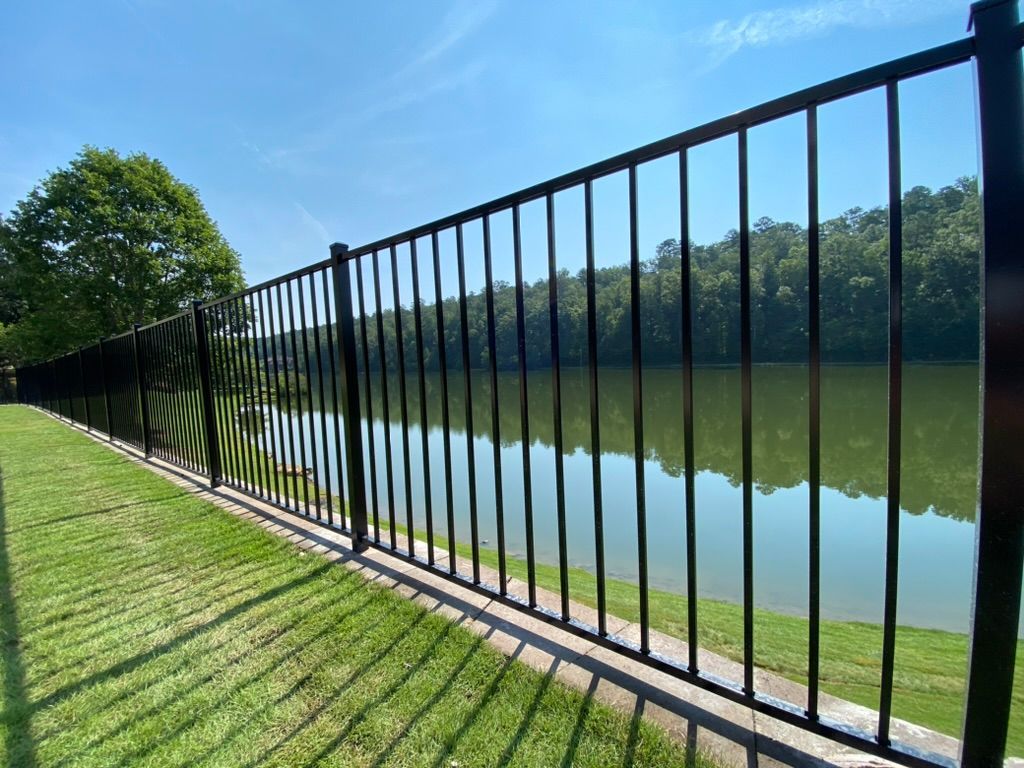 A black metal fence surrounds a lake with trees in the background.
